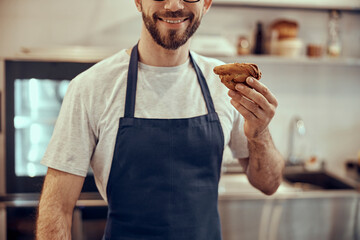 Cheerful male worker in apron holding pastry