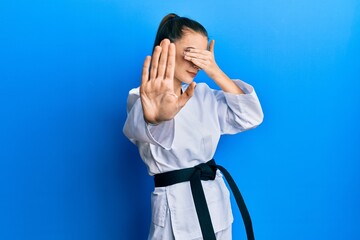 Wall Mural - Beautiful brunette young woman wearing karate fighter uniform with black belt covering eyes with hands and doing stop gesture with sad and fear expression. embarrassed and negative concept.