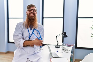 Poster - Young redhead man wearing doctor uniform standing with arms crossed gesture at clinic