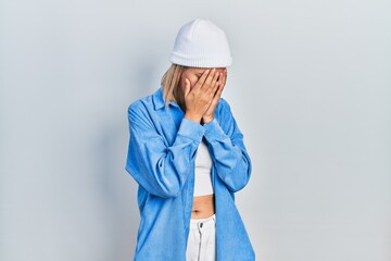 Sticker - Beautiful blonde woman wearing wool hat with sad expression covering face with hands while crying. depression concept.