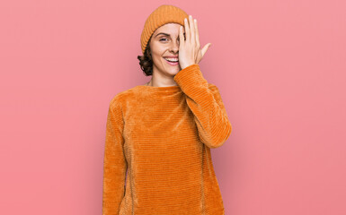 Poster - Young hispanic woman wearing casual clothes and wool cap covering one eye with hand, confident smile on face and surprise emotion.