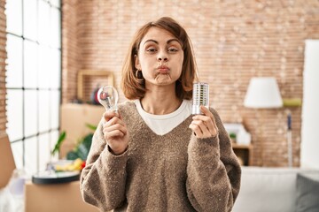 Canvas Print - Young beautiful woman holding led lightbulb and incandescent bulb puffing cheeks with funny face. mouth inflated with air, catching air.