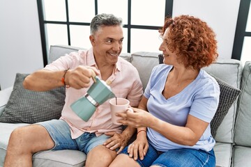 Poster - Middle age man and woman couple drinking coffee sitting on sofa at home