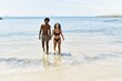 © Krakenimages.com - Young interracial tourist couple wearing swimwear walking with hands together at the beach.