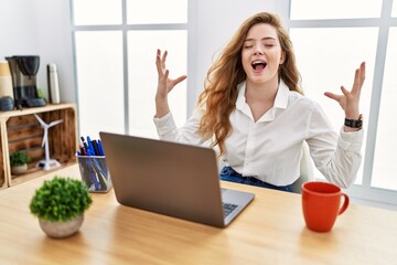 Sticker - Young caucasian woman working at the office using computer laptop celebrating mad and crazy for success with arms raised and closed eyes screaming excited. winner concept