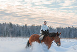 Fototapeta  - A girl in a white cloak rides a brown horse in winter.