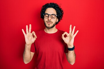 Canvas Print - Handsome hispanic man wearing casual t shirt and glasses relax and smiling with eyes closed doing meditation gesture with fingers. yoga concept.