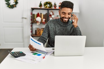 Wall Mural - Young african american man controlling economy using laptop and talking on the smartphone at home.