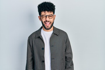 Sticker - Young arab man with beard wearing glasses winking looking at the camera with sexy expression, cheerful and happy face.