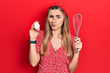 Canvas Print - Beautiful hispanic woman holding egg and baker whisk skeptic and nervous, frowning upset because of problem. negative person.