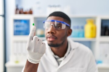 Sticker - Young african american man wearing scientist uniform holding pill at laboratory