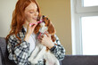© Roman - Redhead young woman in checkered shirt brushing spaniel dog teeth at home. The process of brushing a dogs teeth. Stay home. Pet care.Good-looking caucasian lady with pet at weekends, indoors