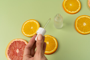 Wall Mural - Natural vitamin C serum, skin care, essential oils. Cosmetic glass bottle fresh juicy slices of oranges and grapefruits. A woman's hand holds a pipette.