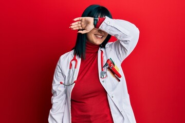 Poster - Young hispanic woman wearing doctor uniform and stethoscope covering eyes with arm smiling cheerful and funny. blind concept.