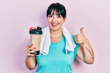 Sticker - Young hispanic woman wearing sport clothes drinking a protein shake smiling happy and positive, thumb up doing excellent and approval sign