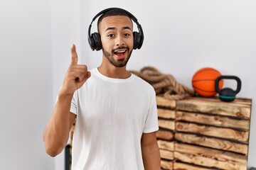 Poster - African american man listening to music using headphones at the gym pointing finger up with successful idea. exited and happy. number one.