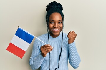 Canvas Print - African american woman with braided hair holding france flag screaming proud, celebrating victory and success very excited with raised arm