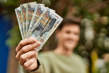 Young hispanic man smiling happy holding peruvian soles banknotes at the city.