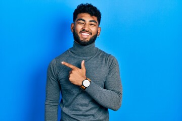 Poster - Arab man with beard wearing turtleneck sweater cheerful with a smile on face pointing with hand and finger up to the side with happy and natural expression