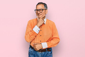 Poster - Middle age indian man wearing casual clothes and glasses with hand on chin thinking about question, pensive expression. smiling with thoughtful face. doubt concept.