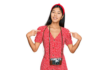 Poster - Beautiful young asian woman wearing dress and vintage camera looking confident with smile on face, pointing oneself with fingers proud and happy.