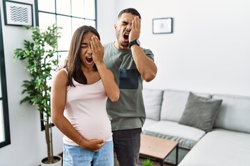 Wall Mural - Young interracial couple expecting a baby, touching pregnant belly yawning tired covering half face, eye and mouth with hand. face hurts in pain.