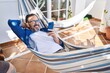 Middle age man using smartphone lying on hammock at terrace home