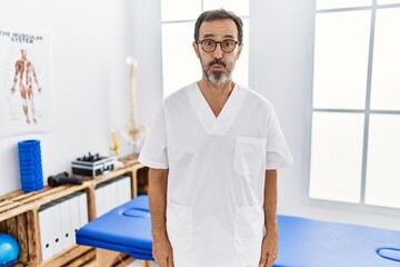 Poster - Middle age man with beard working at pain recovery clinic puffing cheeks with funny face. mouth inflated with air, crazy expression.