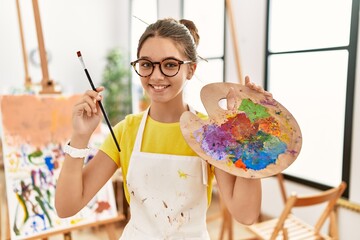 Wall Mural - Adorable girl smiling confident holding paintbrush and palette at art studio