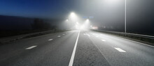 Panoramic View Of The Illuminated New Highway In A Fog At Night, Street Lights Close-up. Moonlight. Dark Urban Scene. Europe. Transportation, Logistics, Travel, Tourism, Road Trip, Freedom, Driving