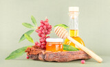 Fototapeta Sypialnia - Fresh honey in glass jar, honey dipper, bottle with natural oil, branches of red berries with green leaves on a pastel green background, front view, close-up. Healthy eating, good food.