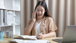 © Puwasit Inyavileart - Asian female worker talking on phone and working on laptop with smiling face, Office staff work and telephone conversations, Take notes for reminders, Business conversation over the phone.