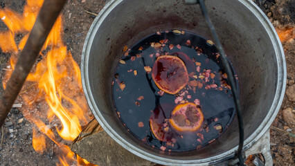 Wall Mural - Mulled wine in a tourist pot over hot camp fire. Mulled wine by the fire. Mulled wine cooked on fire outdoors. Picnic.