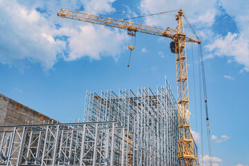 Construction crane with a new steel structure building. Against the background of a blue sky with clouds.