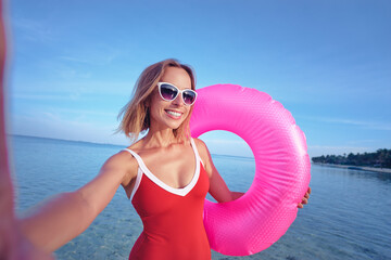 Wall Mural - Technology and vacation. Pretty young woman in swimsuit taking selfie on the beach.