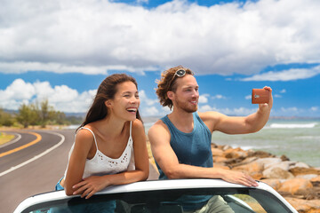 Road trip vacation sports car people taking phone pictures of Hawaii landscape on summer travel trip. Tourists couple taking photos with smartphone camera app. Happy Asian woman