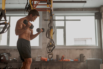 Wall Mural - Athletic young man holding dumbbells in hands and doing exercise to strengthen his biceps in fitness center