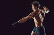 Side view of aggressive muscular boxer who strikes isolated on dark background. Sport concept