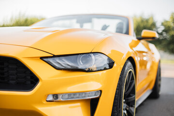 Particle view of yellow brand new modern luxury sport car parked outdoors. Headlights and hood of sport yellow car. Car detail