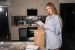 © Andrii Lysenko - A beautiful caucasian woman in the evening at home takes out disposable boxes for dinner with food from a paper eco bag. Takeaway food concept