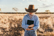 © Austockphoto - Cowgirl in blue long sleeves holding tablet in paddock