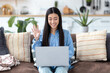 © kucherav - Smiling Asian woman using laptop for chatting online sitting on the sofa at home or in a modern office. Internet, social network communication, video call concept