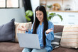 © kucherav - Smiling Asian woman using laptop for chatting online sitting on the sofa at home or in a modern office. Internet, social network communication, video call concept