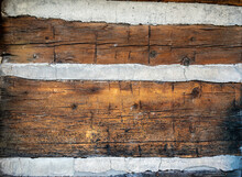 A Closeup Of An Exterior Wall Of An Historic Log Cabin, Showing Aged Wood, Horizontal Planks And Cement Grout Between The Logs.