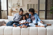 © fizkes - Happy friendly young African American couple parents and small adorable kids son daughter using different gadgets, playing games, web surfing, spending time online or shopping, modern tech addiction.