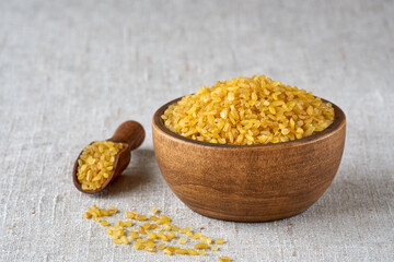 Wall Mural - Uncooked bulgur in wooden bowl on linen cloth background. Bulgur wheat grains .Closeup