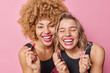 © WHstudio Leushin N - Joyful female models apply lisptick smile broadly have fun while doing makeup prepare for party laugh out happily wear black t shirts isolated over pink background. Women and beauty procedures