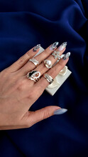 Many Rings On A Beautiful Female Hand On Each Finger On The Background Of Dark Blue Fabric Top View. Five Rings On A Woman's Hand. Silver And Gold Rings With Diamonds, Silver Ring, Diamond Ring