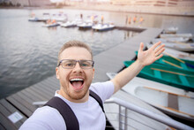 Happy Male Traveler Makes Selfie Photo On Background Of Catamarans Parking Sun Light. Concept Travel Walk On Sea And Lake