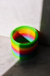 Rainbow color yoyo plastic spiral toy on neutral background lit by sunlight creating shadow.